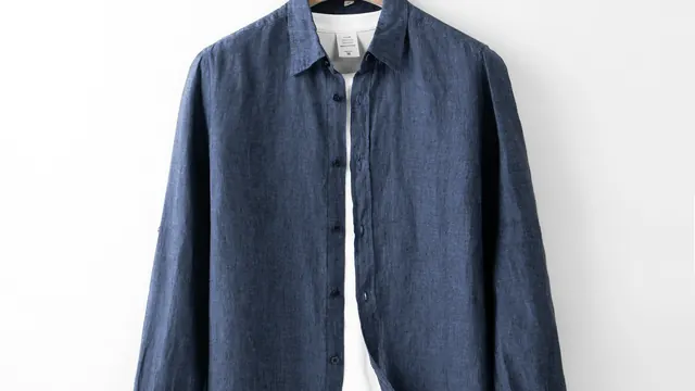 Close view of the collar, buttons and woven fabric of a blue linen shirt