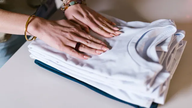 Hands resting on a neat stack of folded white tops and a dark garment