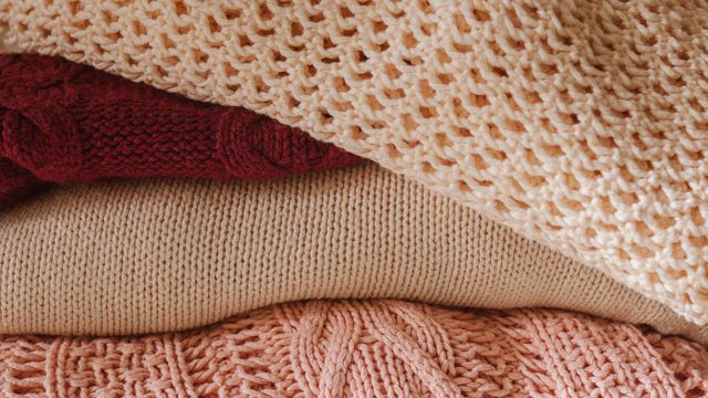 A stack of folded knitted wool and cashmere jumpers in cream, beige, burgundy, and pink.
