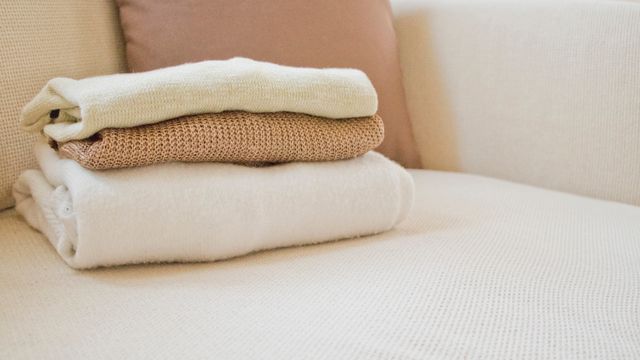 A stack of neatly folded knitted jumpers resting on a cream upholstered chair.