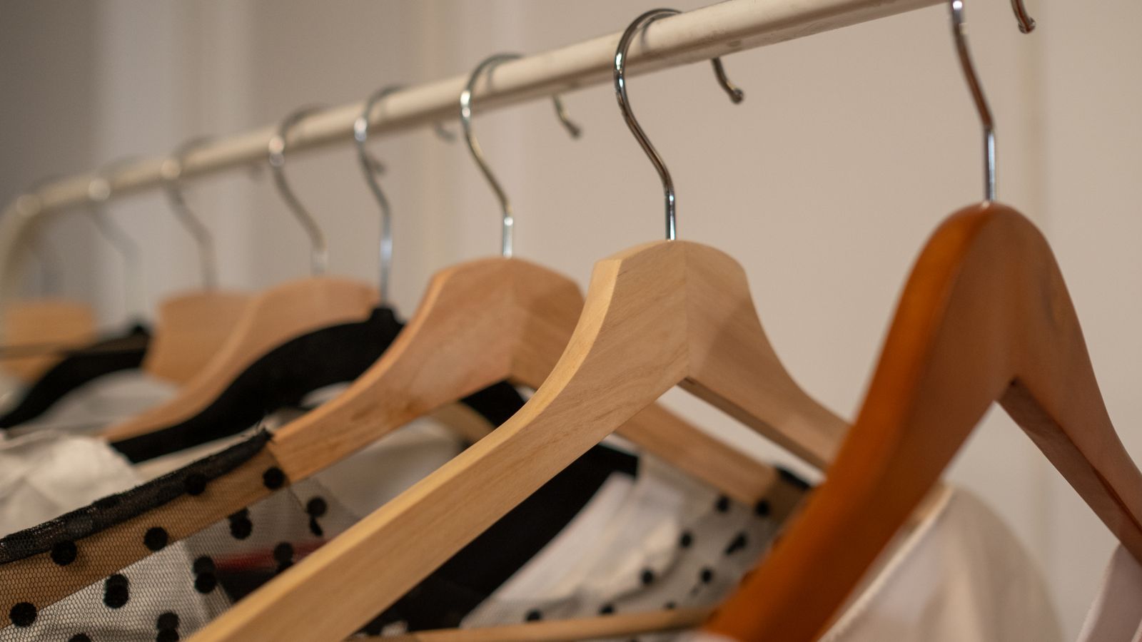 Wooden clothes hangers on a garment rail holding tops and dresses.
