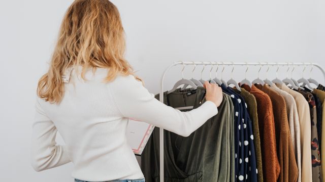 Rear view of a person with blonde wavy hair checking garments hanging on a clothes rail.