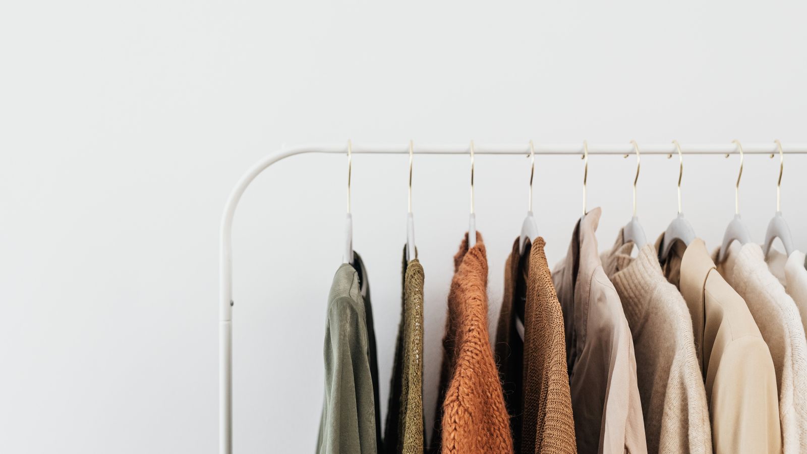 Neutral and earth-toned garments hanging neatly on coat hangers along a minimalist white clothes rail.