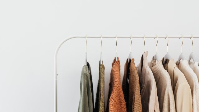Neutral and earth-toned garments hanging neatly on coat hangers along a minimalist white clothes rail.
